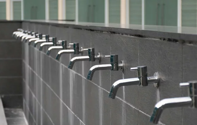 Row of metal ablution taps on a grey wall